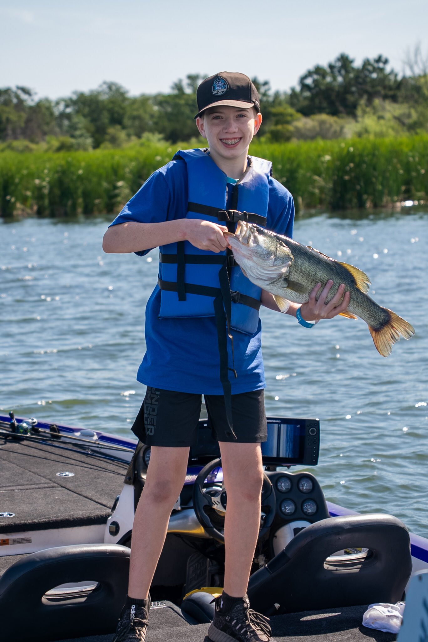 young boy with blue life jacket holding a fish